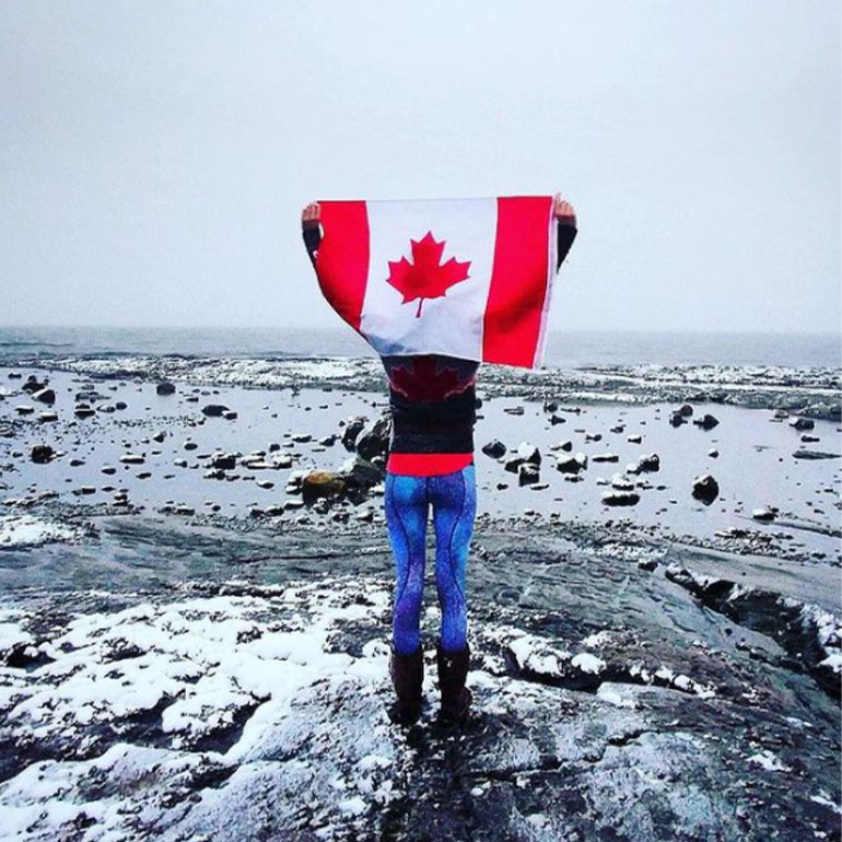 A person holding the Canadian flag up overlooking a body of water